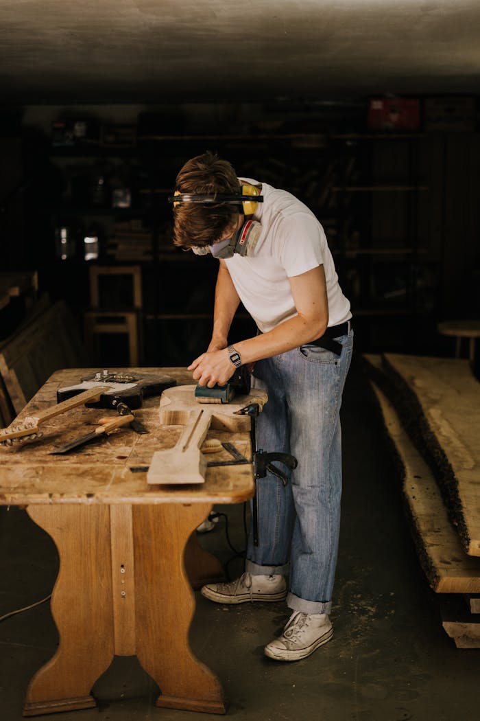 Skilled carpenter sanding a wooden plank in a workshop wearing safety gear.